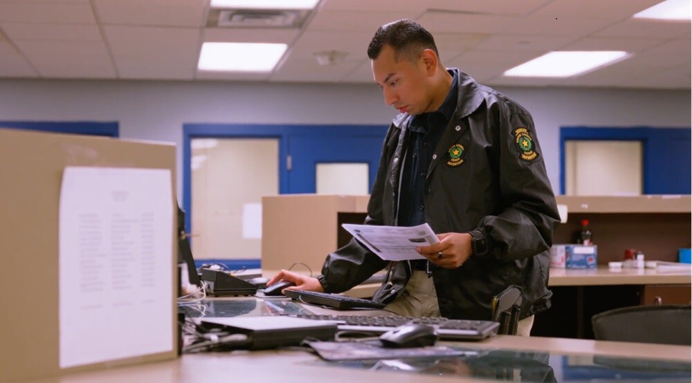 corrections officer on computer looking at paper